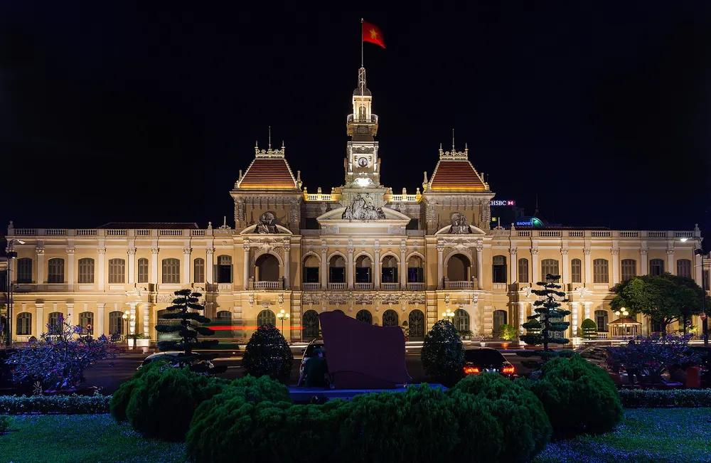 Ho Chi Minh City Hall lit up at night behind a garden