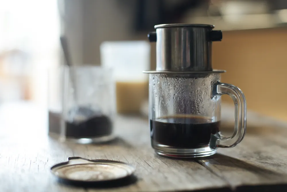 Vietnamese coffee dripping through a metal phin filter into a glass