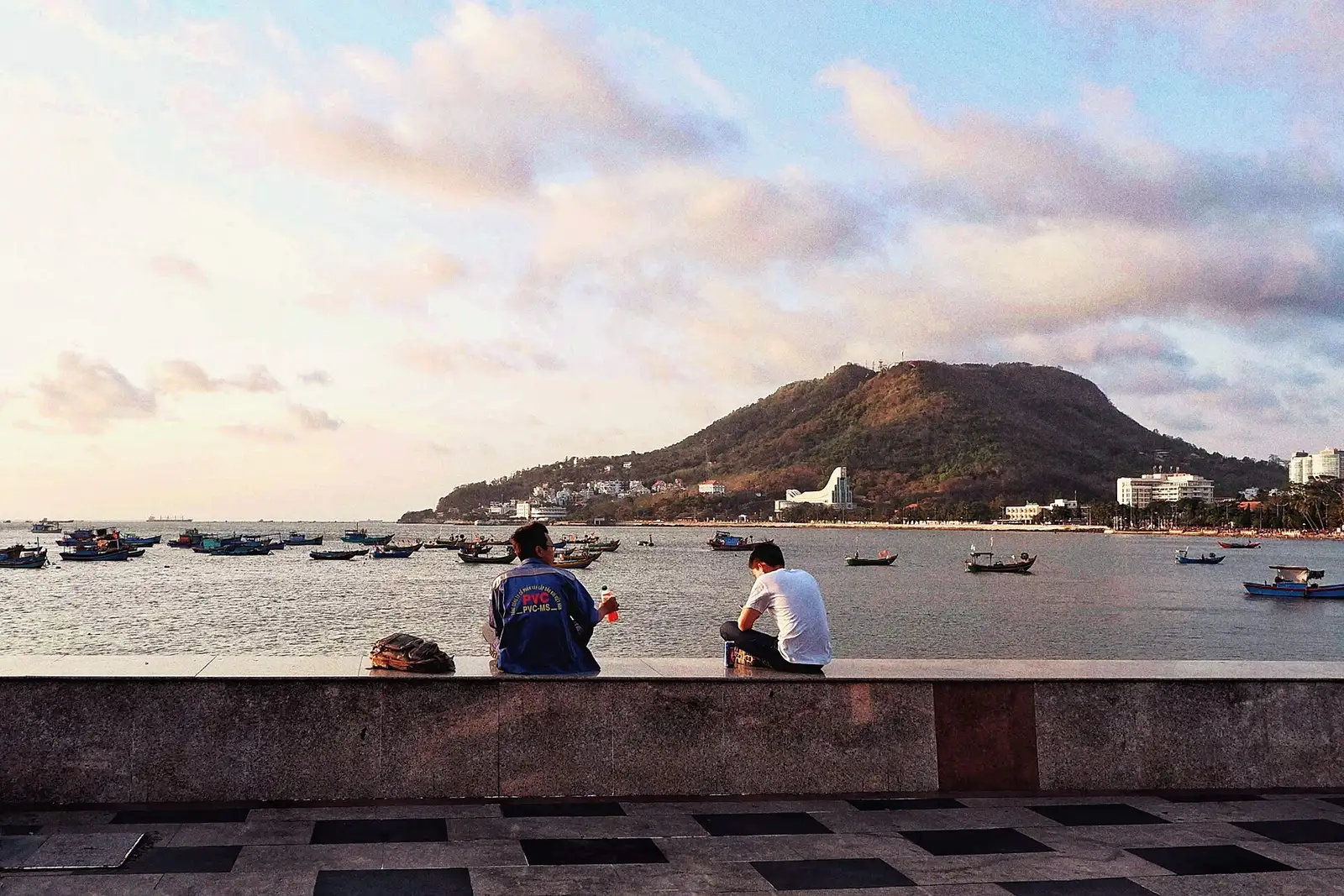 Sunset over the sea and hills in Vũng Tàu, people seen from behind on the seawall