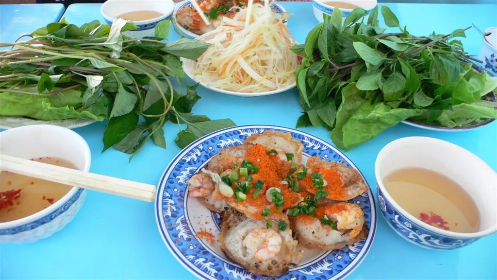 Plate of bánh khọt in Vũng Tàu with fresh herbs, lettuce and dipping sauce