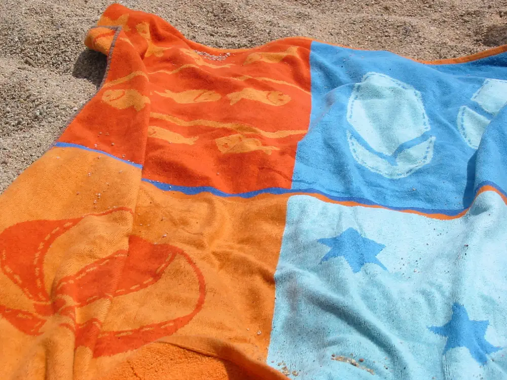 Orange and blue beach towel spread on sand