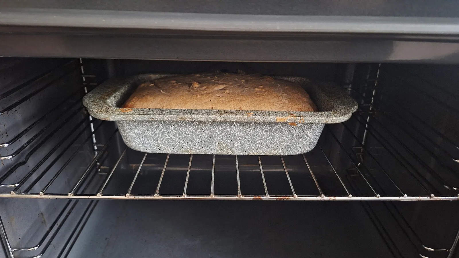 Loaf of bread baking in a tin inside an oven