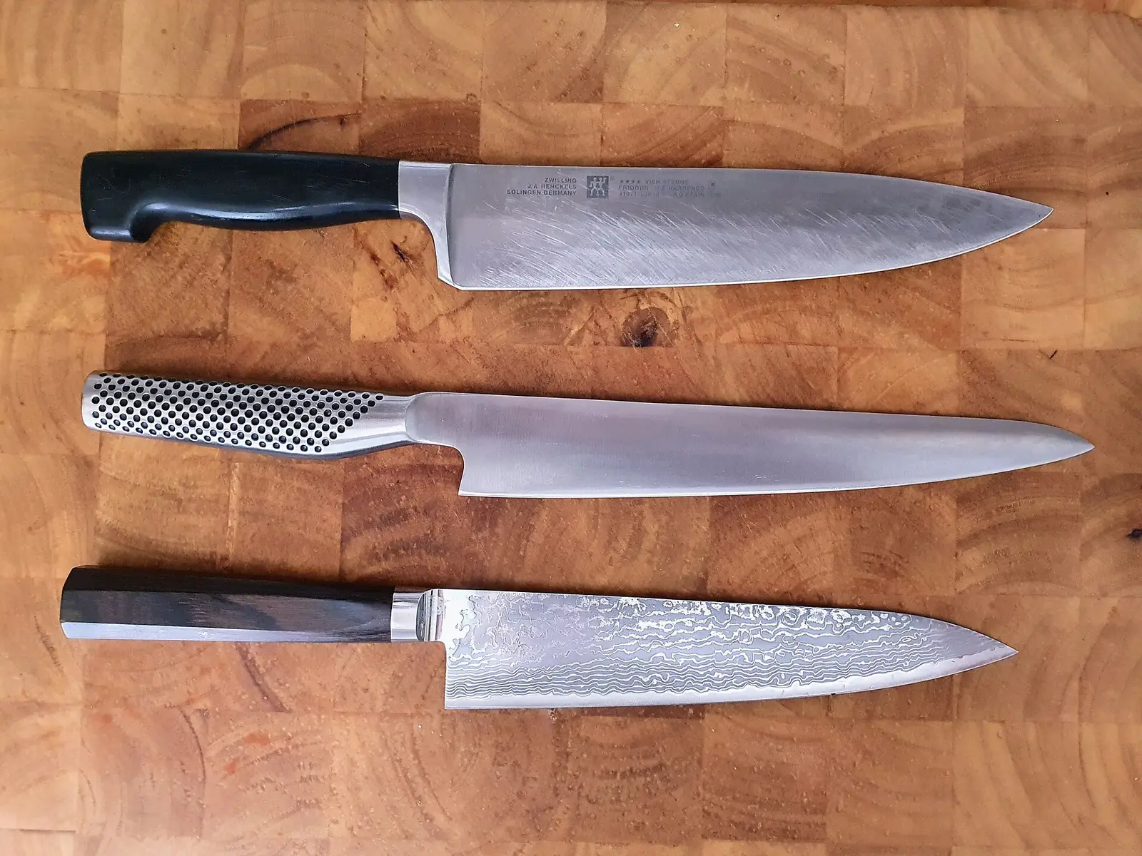 Three chef's knives on a wooden cutting board