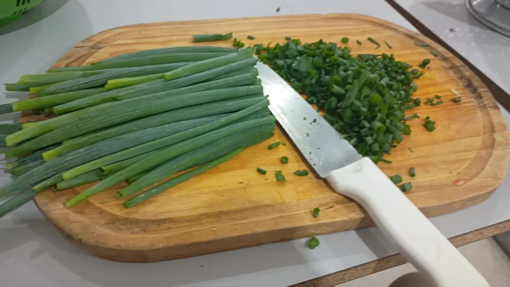 Kitchen knife slicing green onions on a wooden cutting board