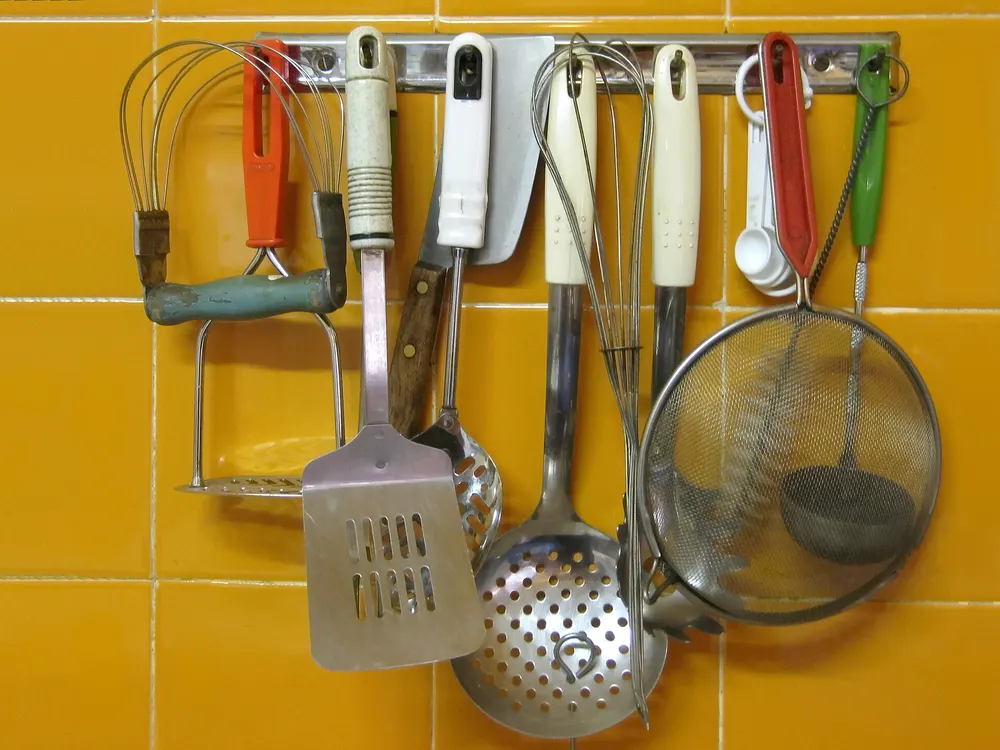 Kitchen utensils hanging on a rail against a yellow tiled wall