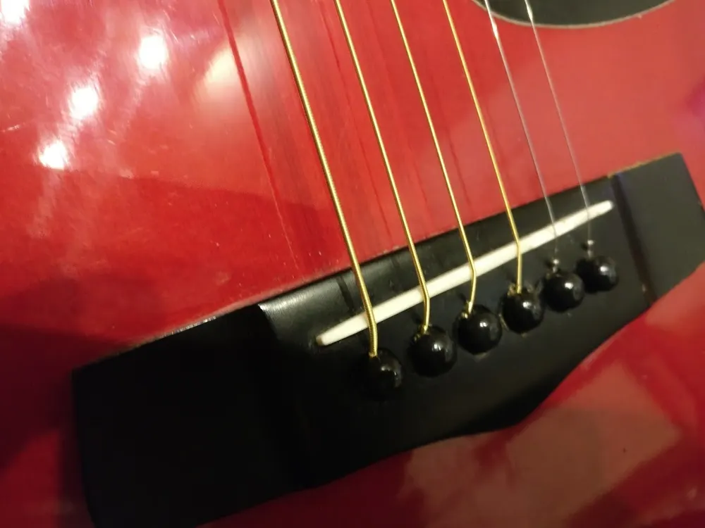 Close-up of the bridge and strings of a red acoustic guitar