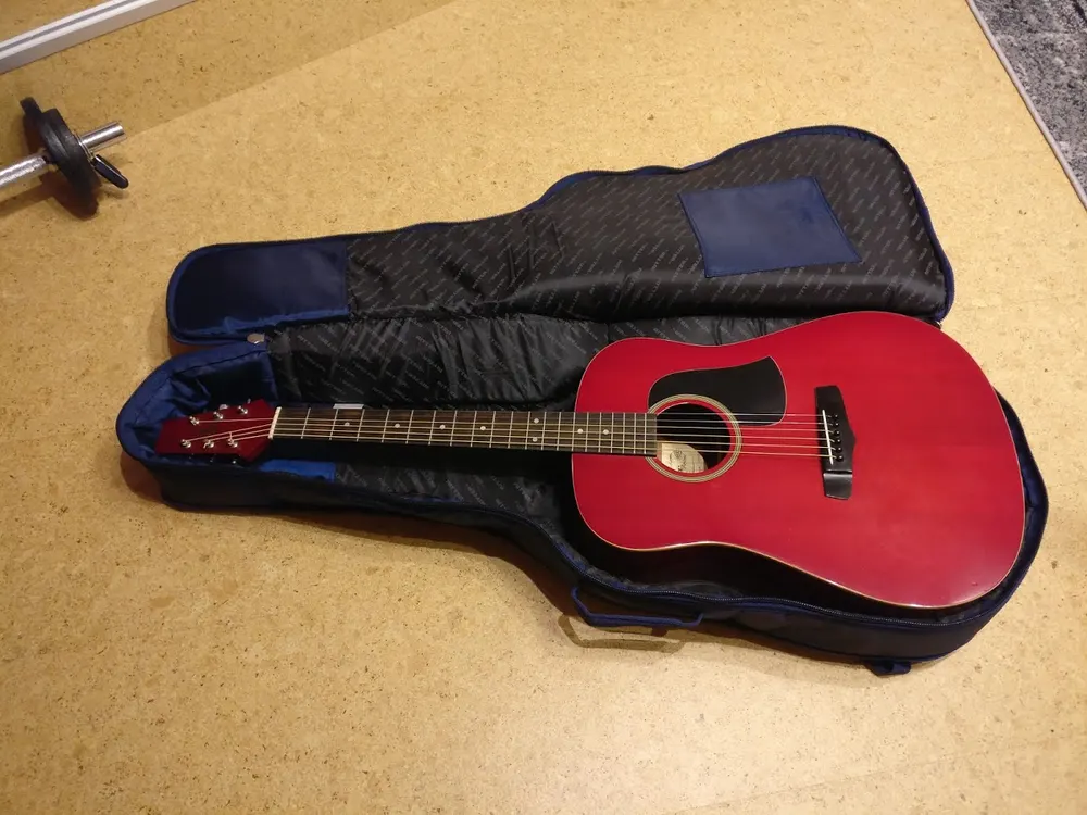 Red acoustic guitar lying in an open padded gig bag