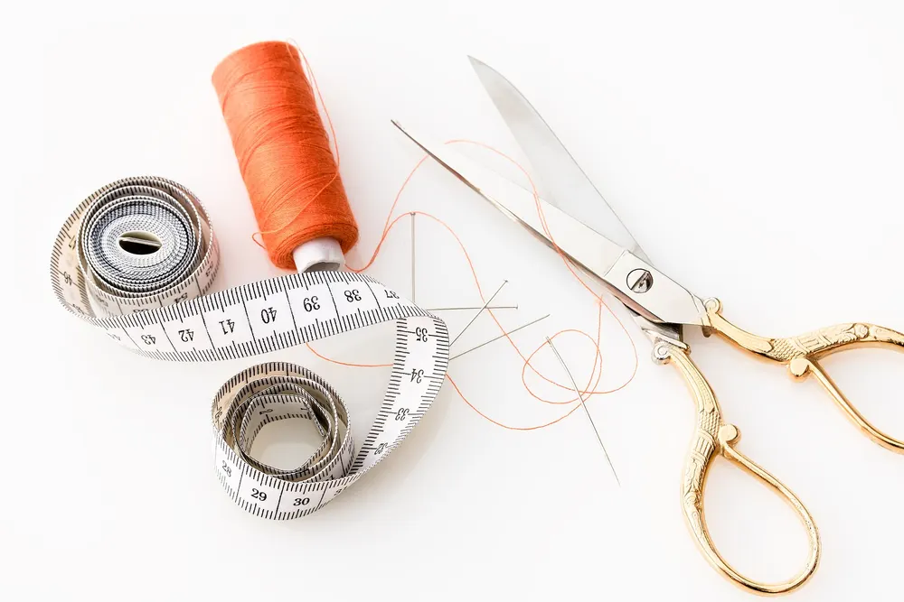 Tape measure, orange thread and sewing scissors on a white surface