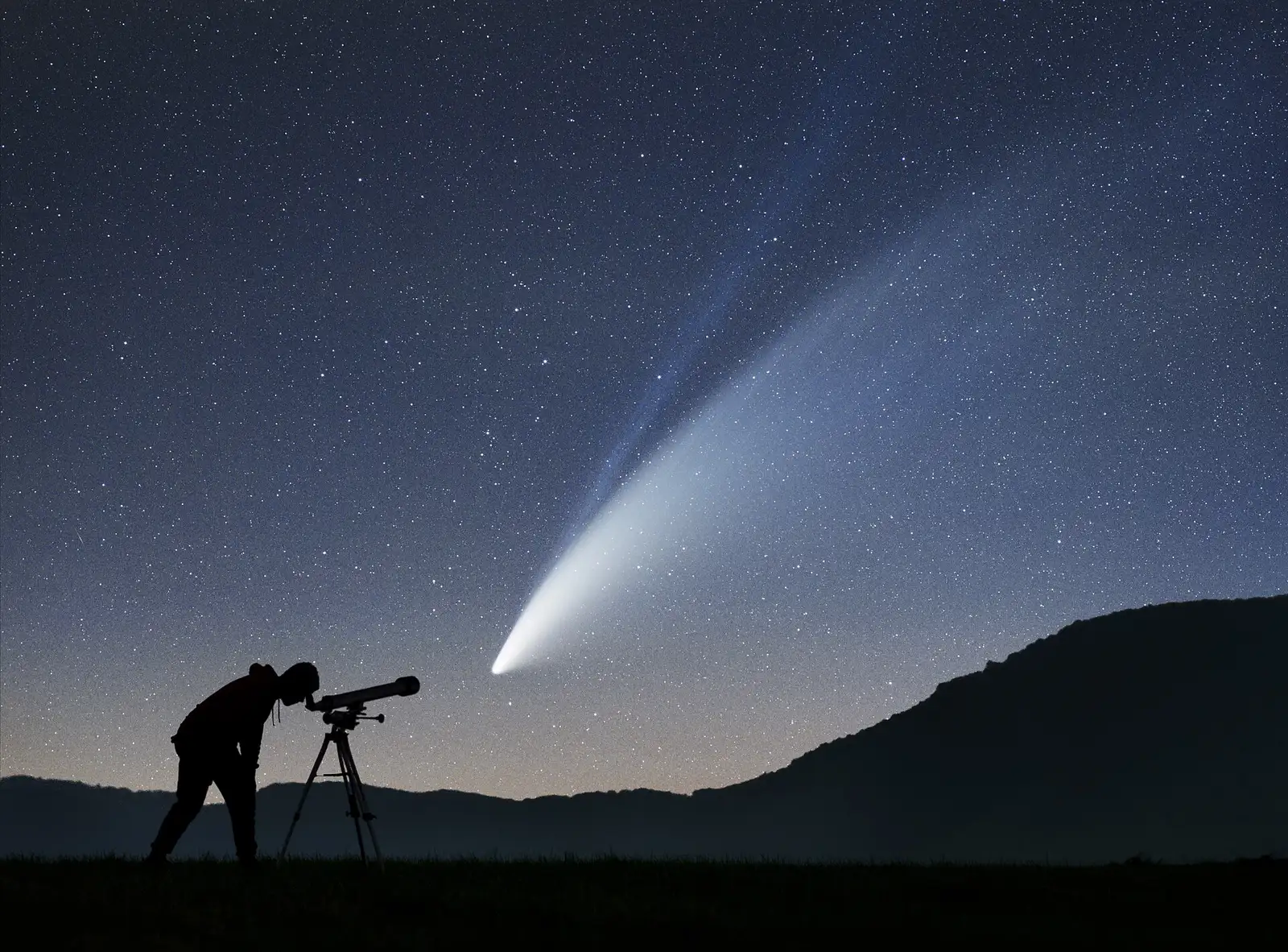 Silhouette of a person with a telescope under a comet in the night sky