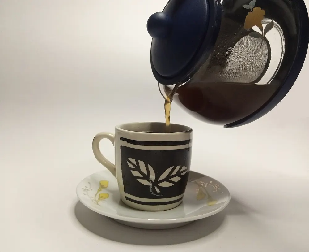 Tea being poured from a teapot into a cup on a saucer