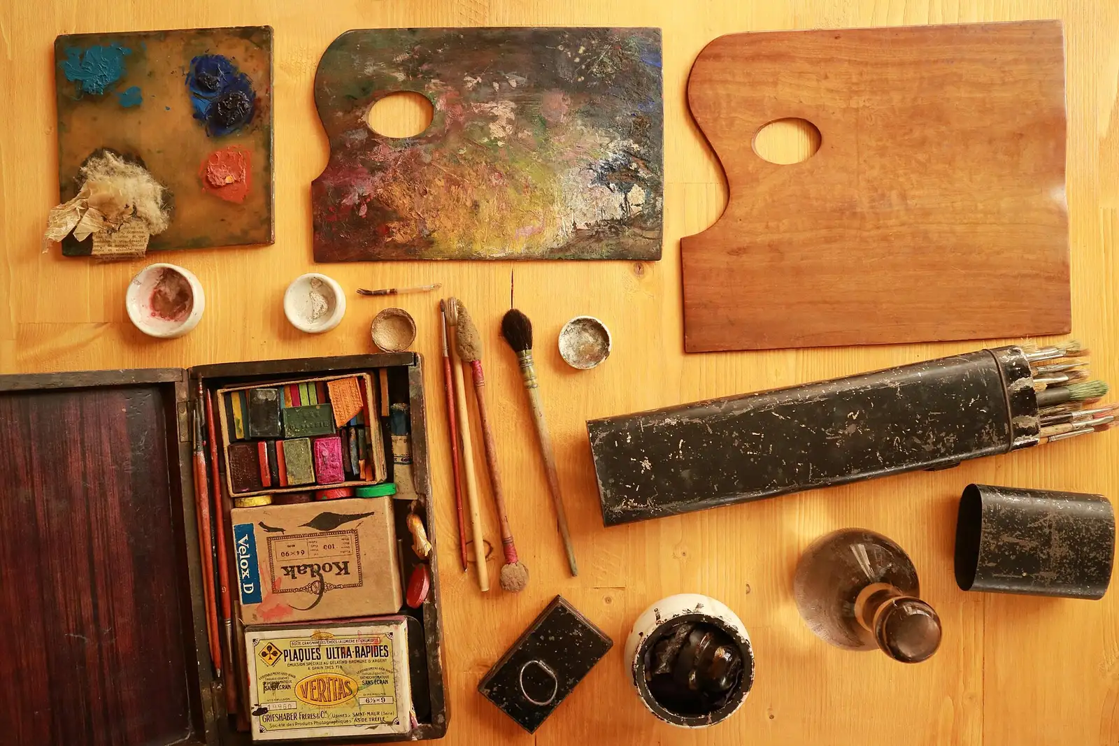 Paint palettes, pastels and brushes laid out on a wooden surface